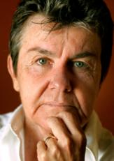 Portrait of a person with short gray-brown hair resting their hand against their chin and looking thoughtfully at the camera.