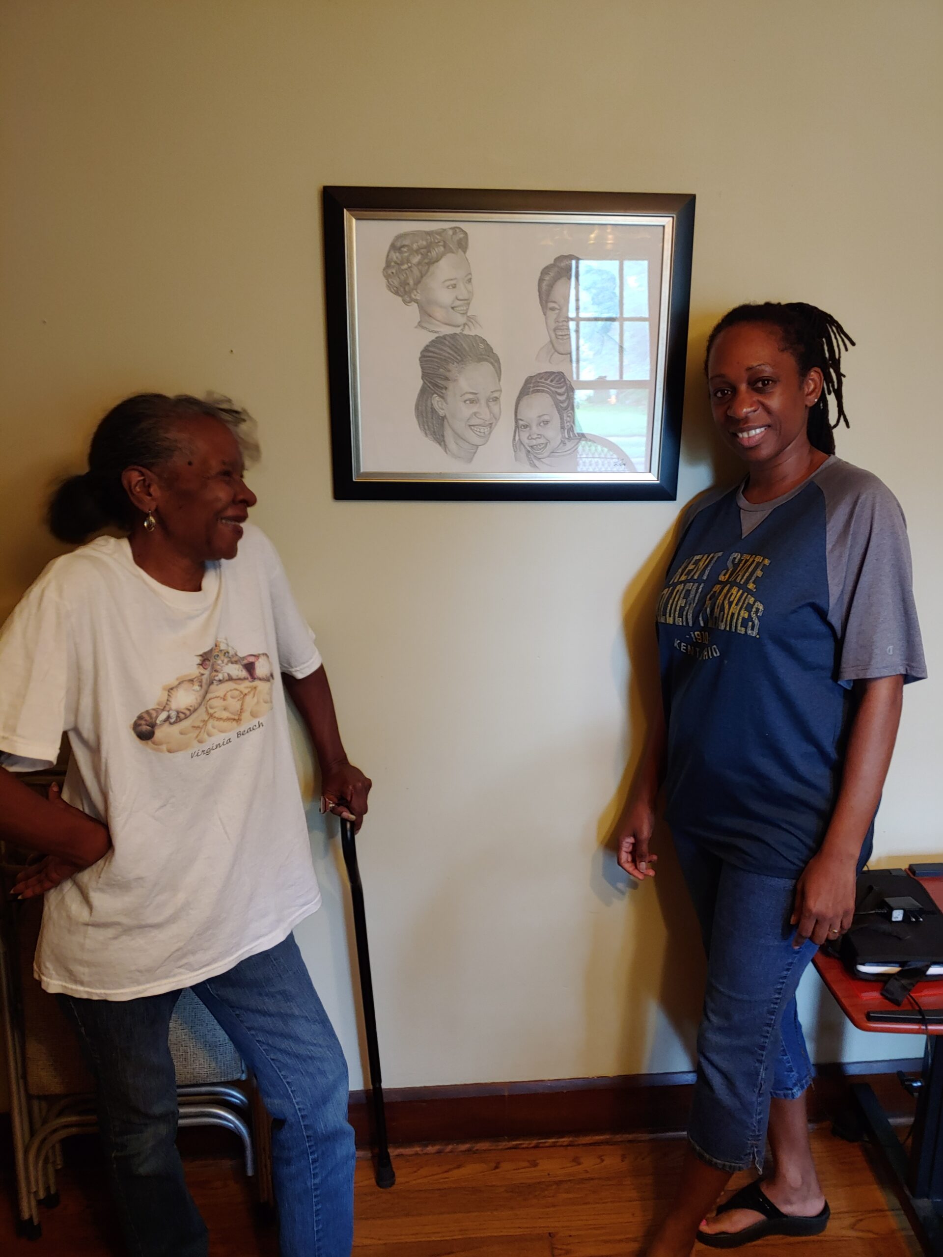 Linda (left) and Shalana (right) pose in front of artwork depicting the four generations of women in their family. 