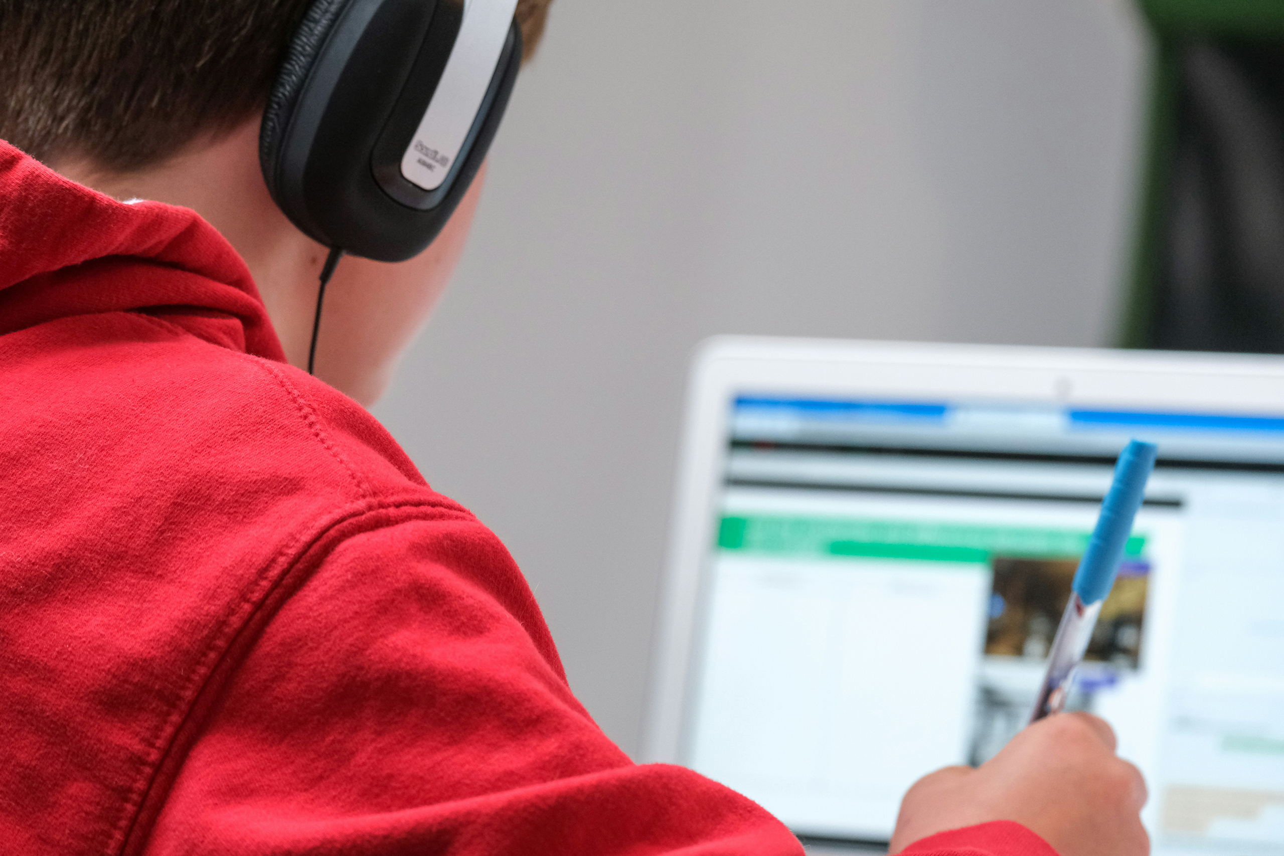 A child wearing headphones and holding a pen sits at a computer