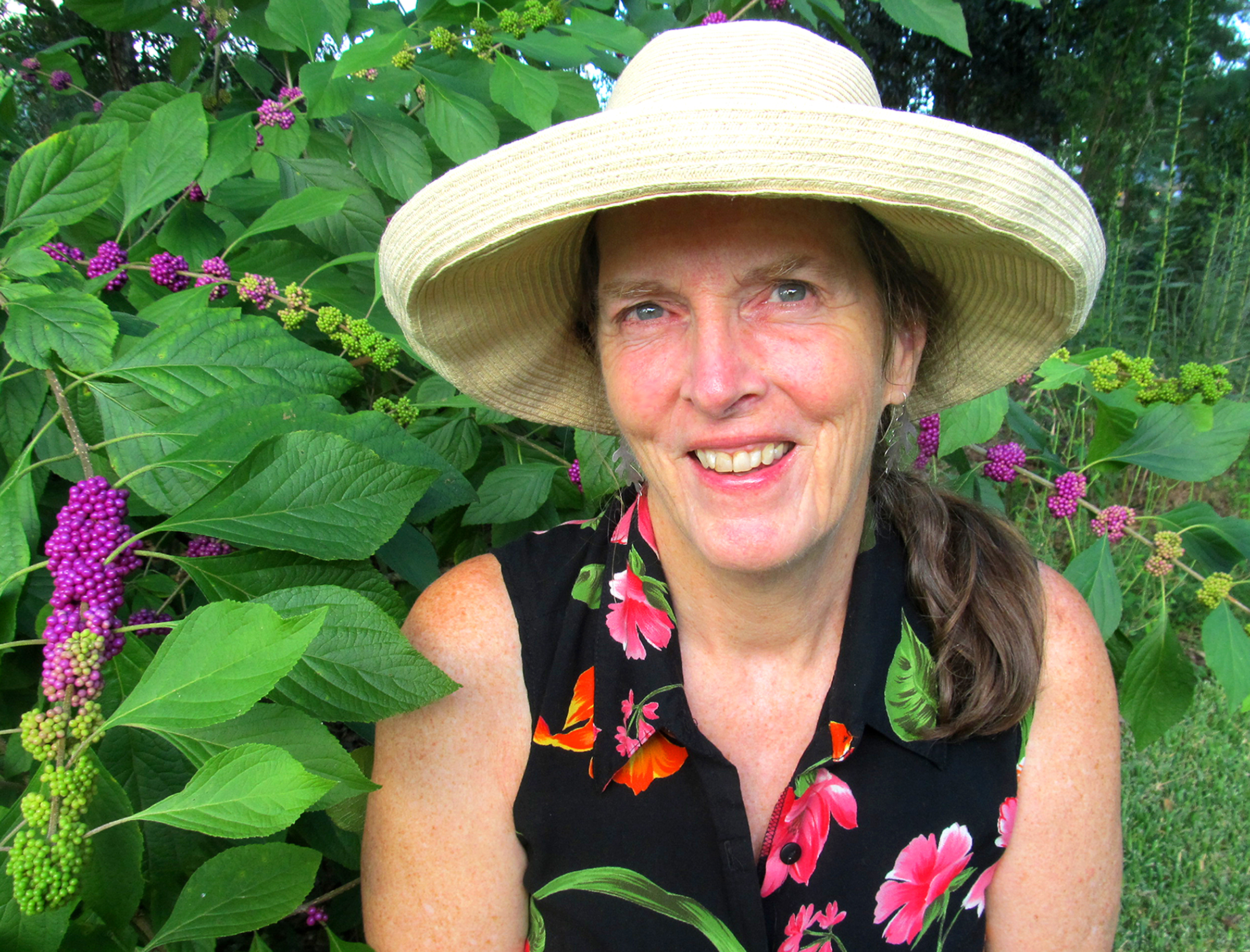 Author photo for Ginny Stibolt. She is wearing a gardening hat and is standing outdoors beside a plant.
