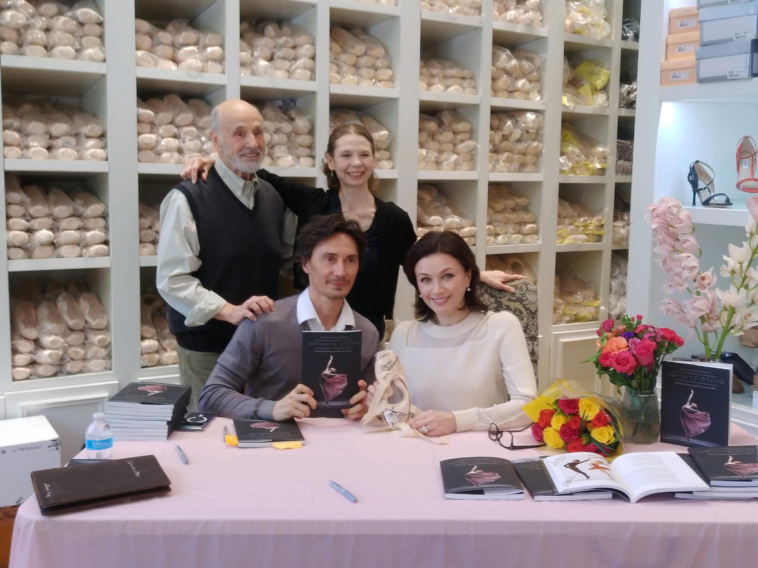 Gene Schiavone and Gavin Larsen pose with featured dancers Irina Dvorovenko and Maxim Beloserkovsky in front of a shelf full of pointe shoes.